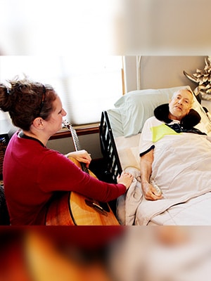 woman playing the guitar to a man in a hospice bed