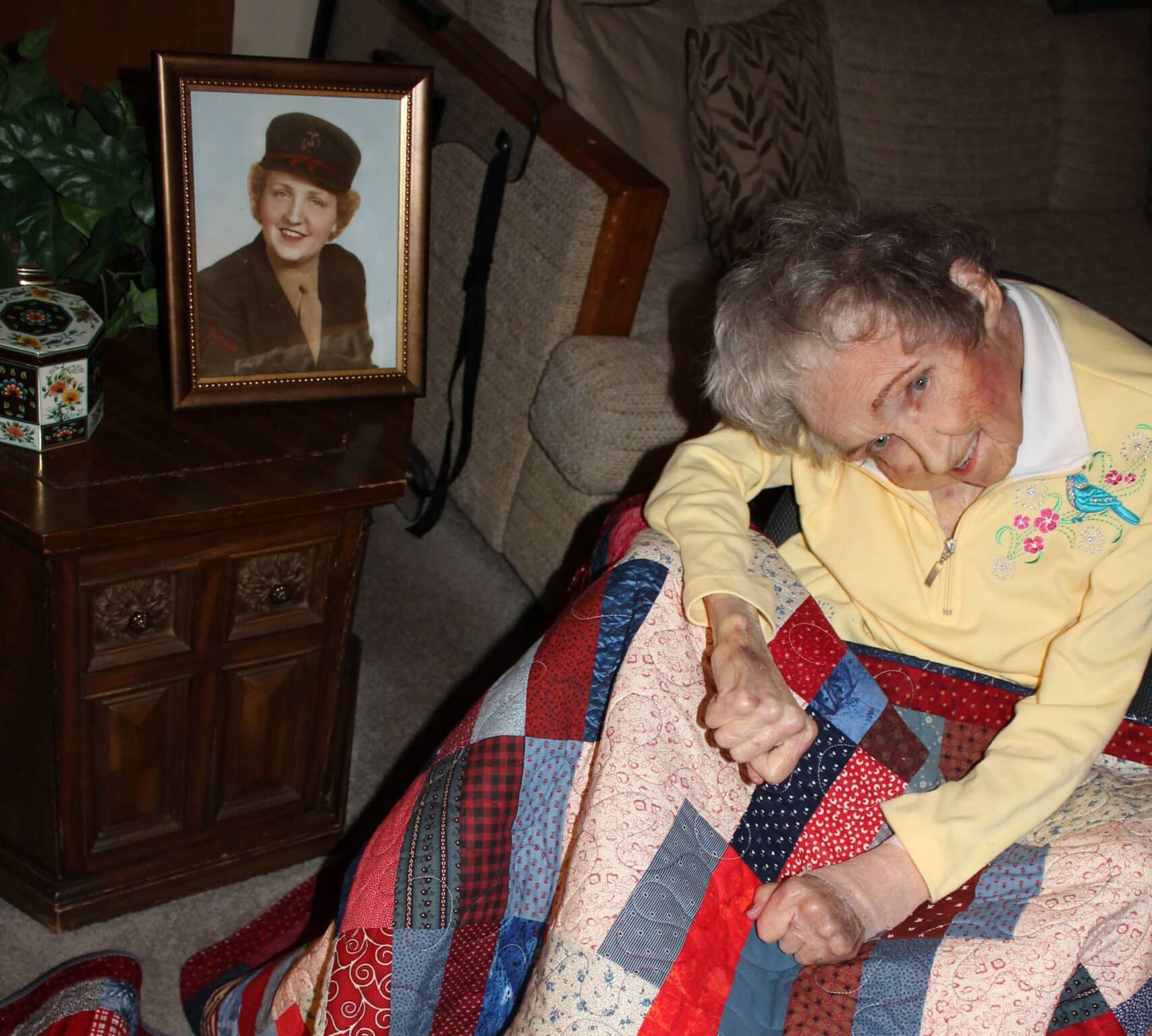 Elderly woman in chair posing next to a young photo of herself