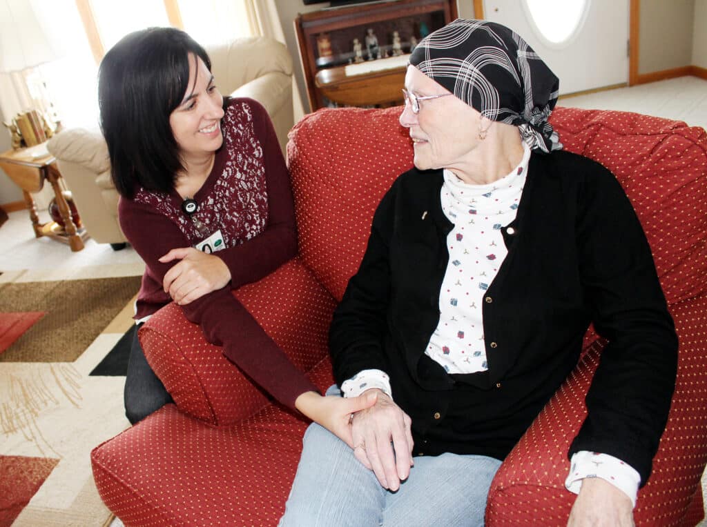 elderly woman sitting in cushioned chair with a nurse kneeling beside talking